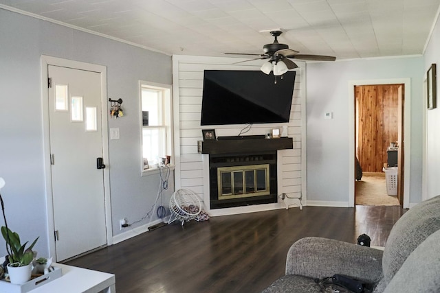 living area with dark wood-style floors, crown molding, a fireplace, ceiling fan, and baseboards