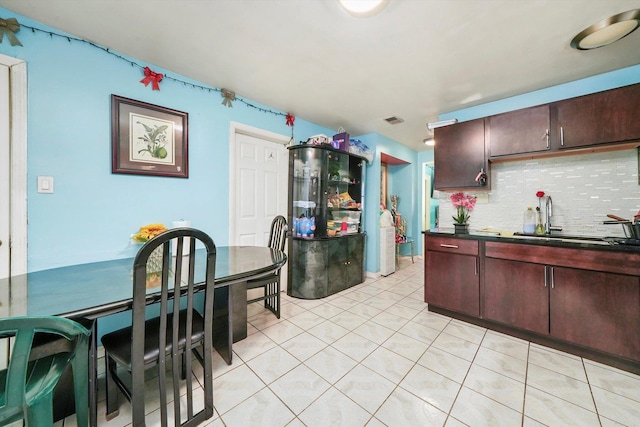 kitchen with light tile patterned floors, dark countertops, decorative backsplash, dark brown cabinetry, and a sink