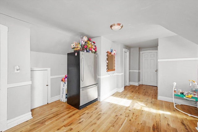 interior space featuring light wood-style flooring, baseboards, vaulted ceiling, and freestanding refrigerator