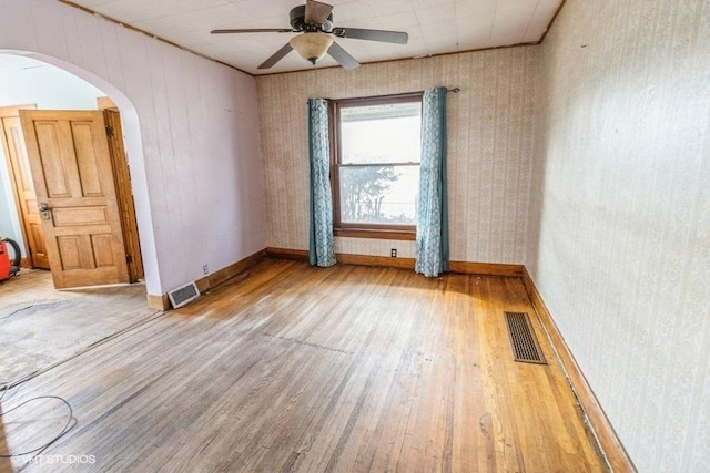 spare room featuring arched walkways, ceiling fan, wood finished floors, and visible vents