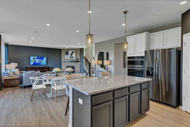 kitchen featuring white cabinets, light stone counters, open floor plan, decorative light fixtures, and stainless steel appliances