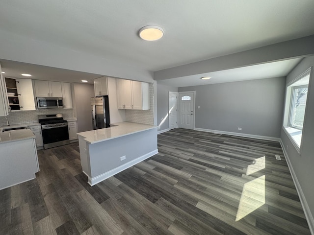 kitchen with light countertops, appliances with stainless steel finishes, white cabinets, a peninsula, and baseboards