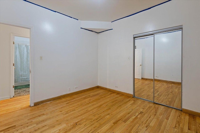 unfurnished bedroom featuring light wood-style floors, baseboards, and a closet