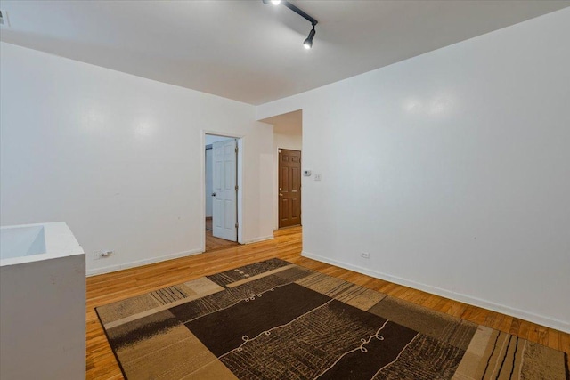 unfurnished bedroom featuring track lighting, visible vents, baseboards, and wood finished floors