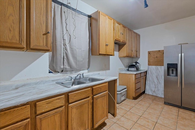 kitchen featuring light tile patterned floors, stainless steel fridge, brown cabinetry, light countertops, and a sink