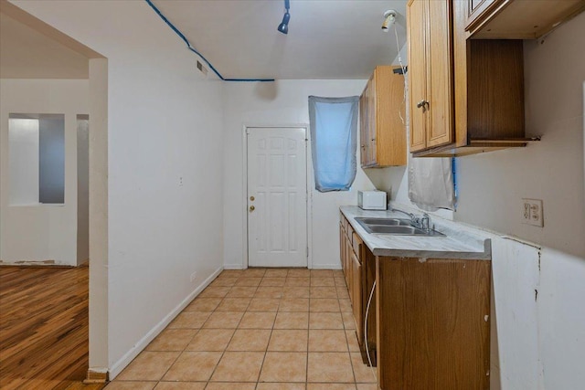 kitchen featuring brown cabinets, light countertops, light tile patterned flooring, a sink, and baseboards