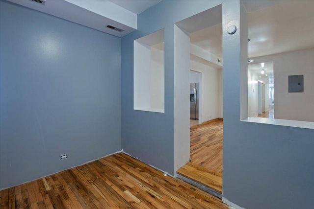 empty room with electric panel, visible vents, and wood finished floors