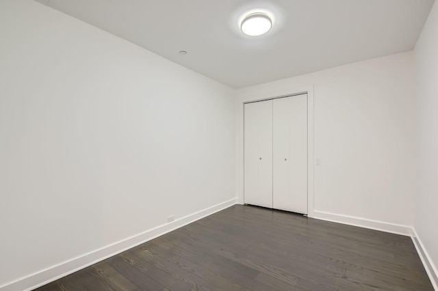 unfurnished bedroom featuring a closet, baseboards, and dark wood-style flooring