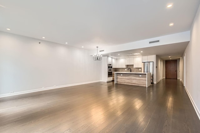 unfurnished living room with dark wood finished floors, an inviting chandelier, baseboards, and visible vents