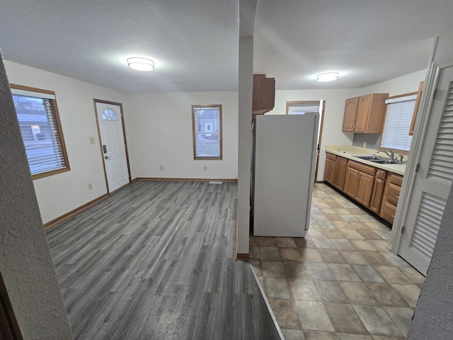 kitchen featuring baseboards, wood finished floors, freestanding refrigerator, light countertops, and a sink