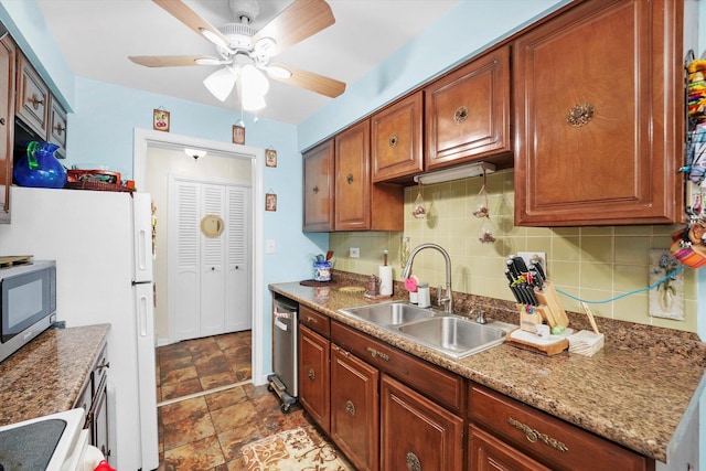 kitchen with backsplash, appliances with stainless steel finishes, a sink, ceiling fan, and dark stone counters