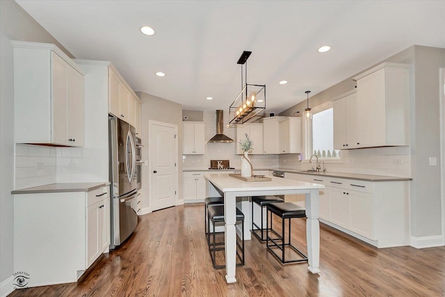 kitchen featuring white cabinets, wall chimney exhaust hood, a breakfast bar, freestanding refrigerator, and a sink