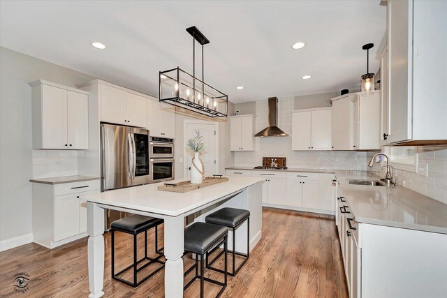 kitchen with a breakfast bar, stainless steel appliances, a sink, wall chimney range hood, and a kitchen island