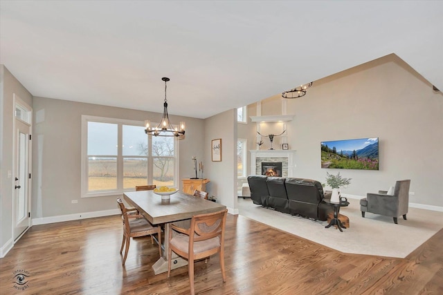 dining area featuring a chandelier, a stone fireplace, baseboards, and wood finished floors