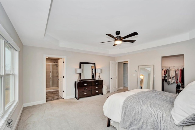 bedroom featuring a tray ceiling, light carpet, ceiling fan, ensuite bath, and baseboards