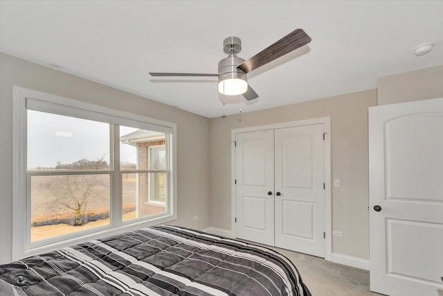 bedroom featuring a ceiling fan, a closet, light colored carpet, and baseboards