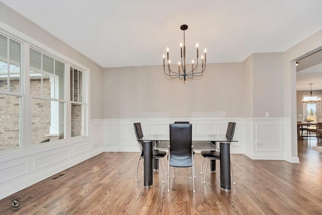 dining area with light wood-style floors, visible vents, a decorative wall, and a notable chandelier