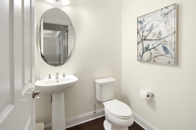 half bathroom featuring baseboards, a sink, toilet, and wood finished floors