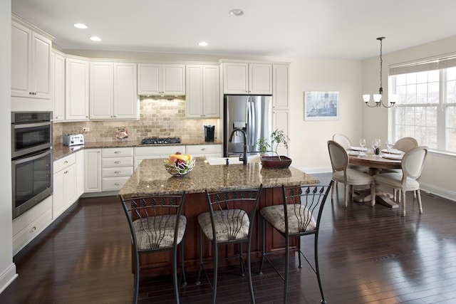 kitchen featuring dark wood finished floors, a breakfast bar area, stainless steel appliances, tasteful backsplash, and white cabinets