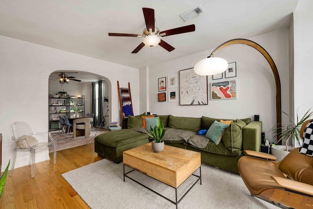 living area with arched walkways, visible vents, light wood finished floors, and ceiling fan