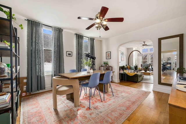 dining space with light wood-style flooring, a ceiling fan, and arched walkways