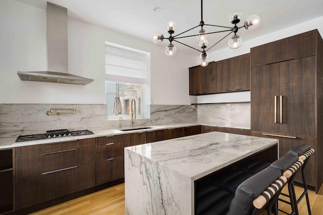 kitchen featuring gas stovetop, a sink, dark brown cabinets, wall chimney exhaust hood, and backsplash