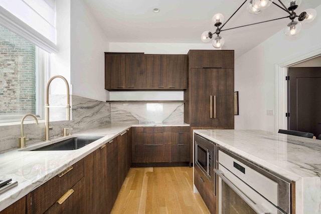 kitchen with light stone countertops, light wood finished floors, a sink, stainless steel microwave, and tasteful backsplash