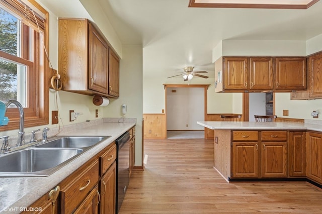 kitchen featuring brown cabinetry, wainscoting, black dishwasher, and a sink