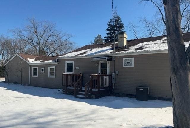 snow covered house featuring a chimney and central AC unit