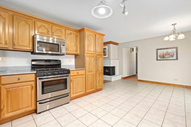 kitchen featuring a warm lit fireplace, light tile patterned floors, baseboards, appliances with stainless steel finishes, and an inviting chandelier