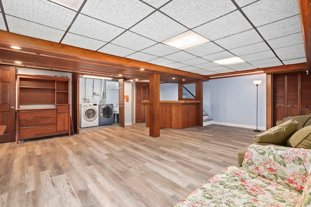 unfurnished living room with baseboards, a drop ceiling, stairway, wood finished floors, and washing machine and dryer