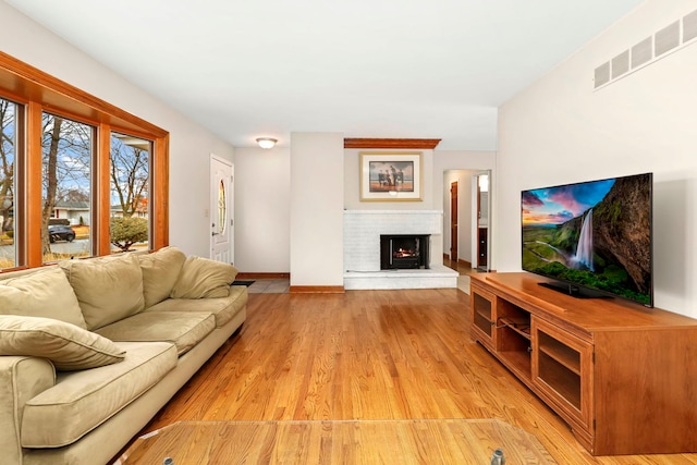 living room featuring a brick fireplace, baseboards, visible vents, and light wood finished floors