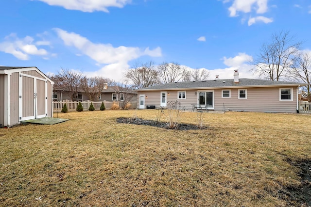 rear view of house with fence, a storage unit, a lawn, and an outdoor structure