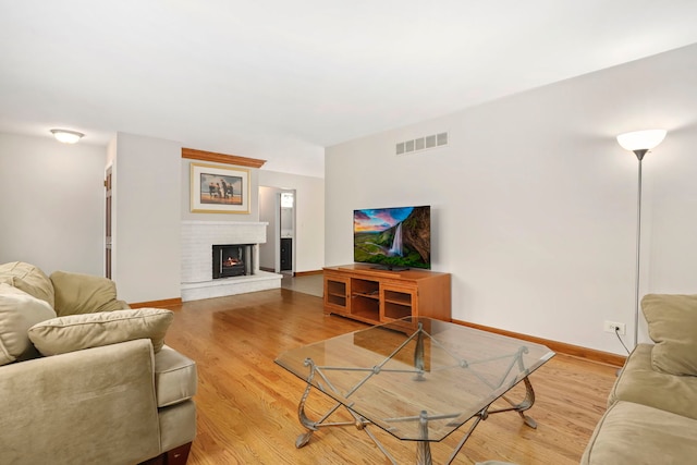 living area with light wood-type flooring, a brick fireplace, visible vents, and baseboards