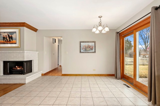 unfurnished dining area featuring a fireplace, visible vents, an inviting chandelier, light tile patterned flooring, and baseboards