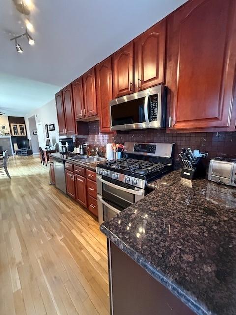 kitchen with stainless steel appliances, tasteful backsplash, a sink, dark stone countertops, and light wood-type flooring