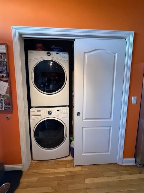 laundry room with stacked washer / drying machine, laundry area, light wood-style flooring, and baseboards