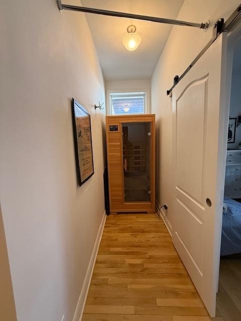 hall featuring light wood finished floors, a barn door, and baseboards