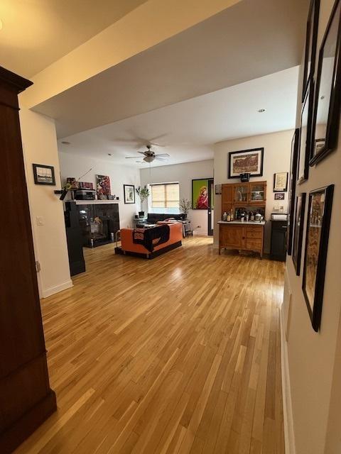 living area featuring ceiling fan, light wood finished floors, a fireplace, and baseboards