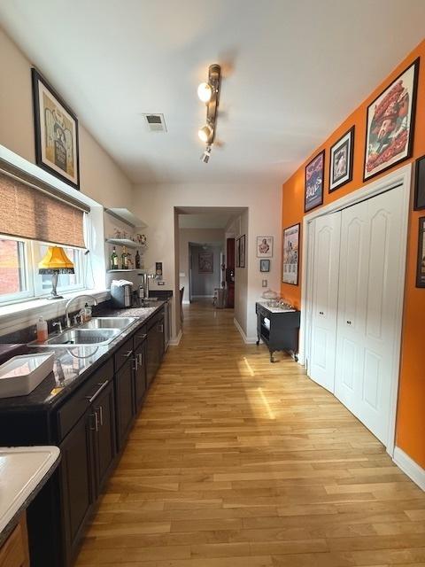 kitchen featuring light wood finished floors, open shelves, visible vents, a sink, and baseboards