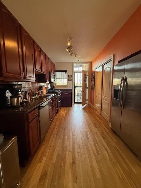 kitchen with light wood finished floors, stainless steel appliances, dark countertops, decorative backsplash, and a sink