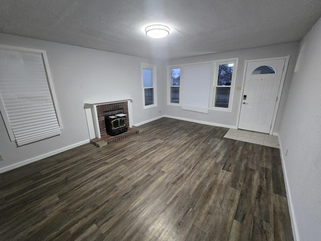 unfurnished living room featuring dark wood-style floors, a wood stove, a textured ceiling, and baseboards