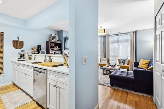 kitchen featuring white cabinetry, open floor plan, dishwasher, and light countertops