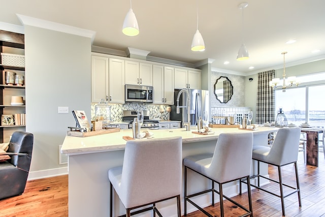 kitchen with a center island with sink, a kitchen breakfast bar, stainless steel appliances, and decorative light fixtures