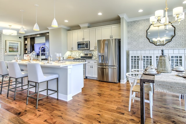 kitchen with a notable chandelier, white cabinetry, appliances with stainless steel finishes, a center island with sink, and pendant lighting