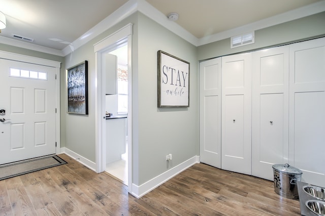 foyer entrance featuring ornamental molding, visible vents, and wood finished floors