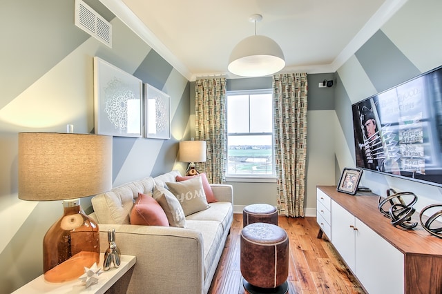 living room featuring light wood-style floors, baseboards, visible vents, and ornamental molding