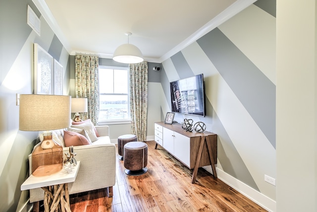 sitting room with light wood-type flooring, baseboards, visible vents, and ornamental molding