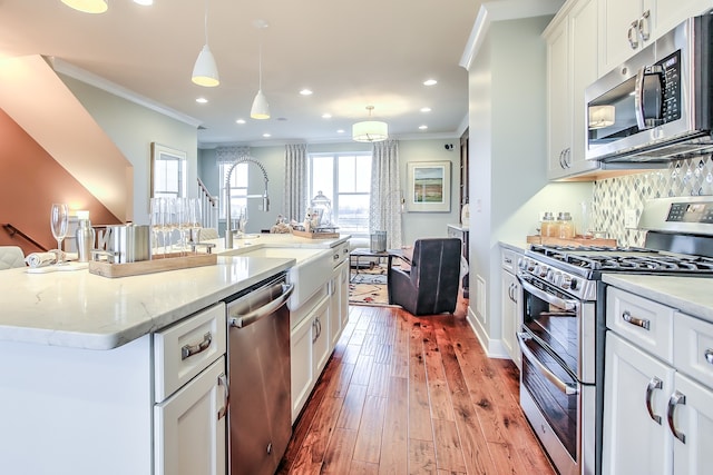 kitchen with an island with sink, light stone countertops, pendant lighting, and stainless steel appliances