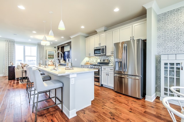 kitchen with pendant lighting, a center island with sink, stainless steel appliances, open floor plan, and white cabinets